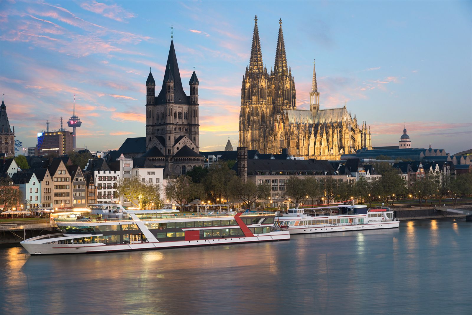 River cruise boats moored on the Rhine below Cologne Cathedral at dusk