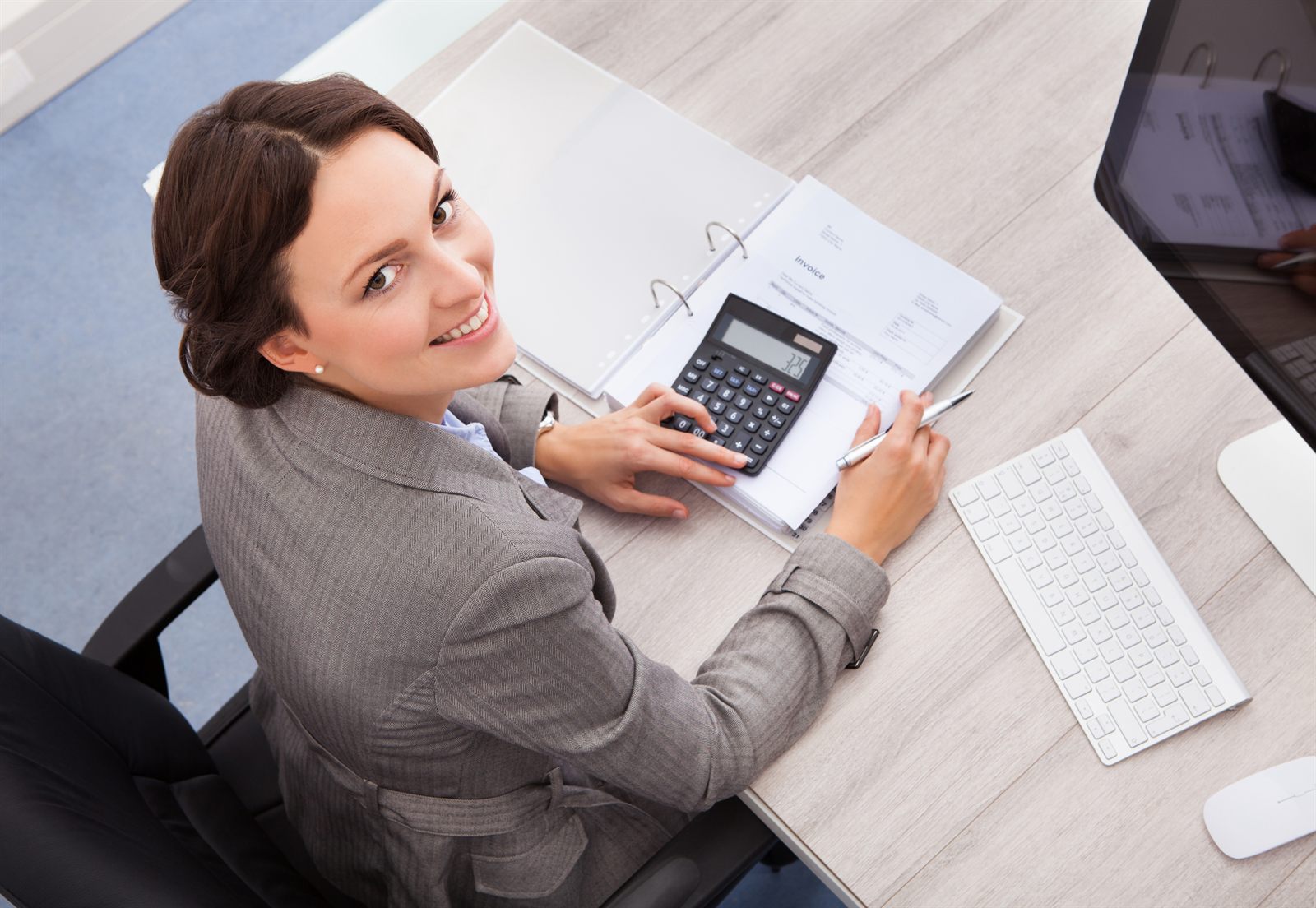 Smiling woman working out figures with a calculator at her desk